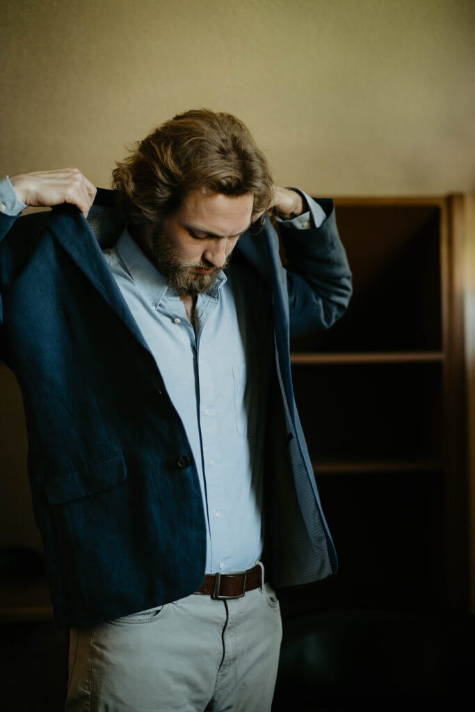 Groom putting on blue velvet suit jacket for elopement styled shoot