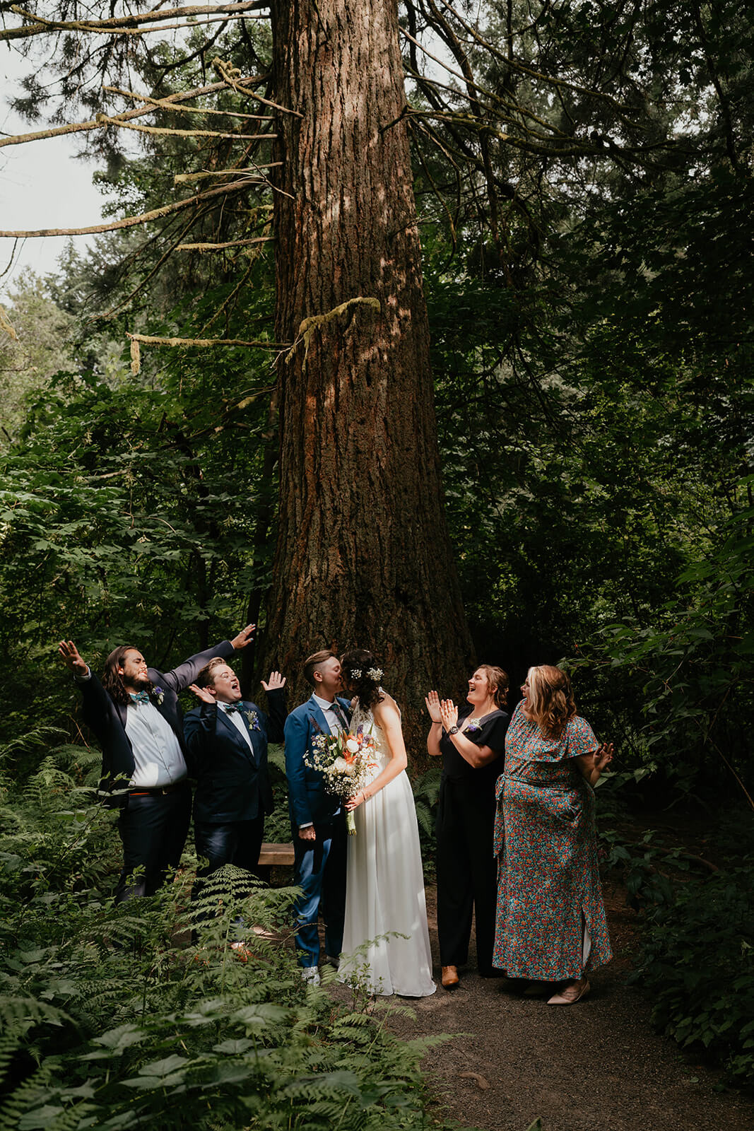 Two brides kiss while wedding party cheers