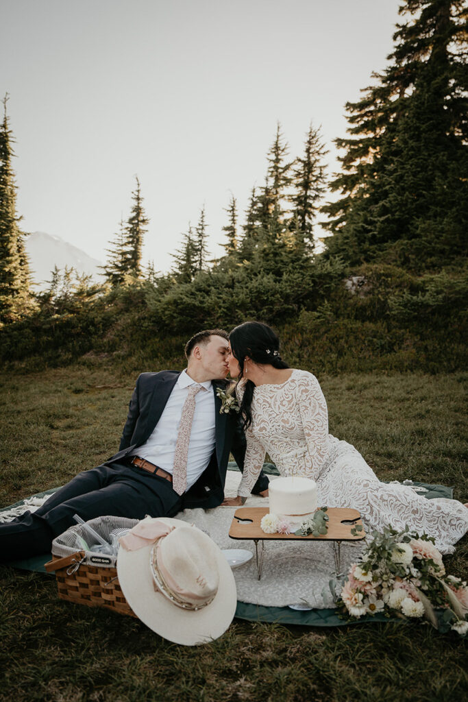 the newlyweds kissing while sitting on a picnic blanket. 