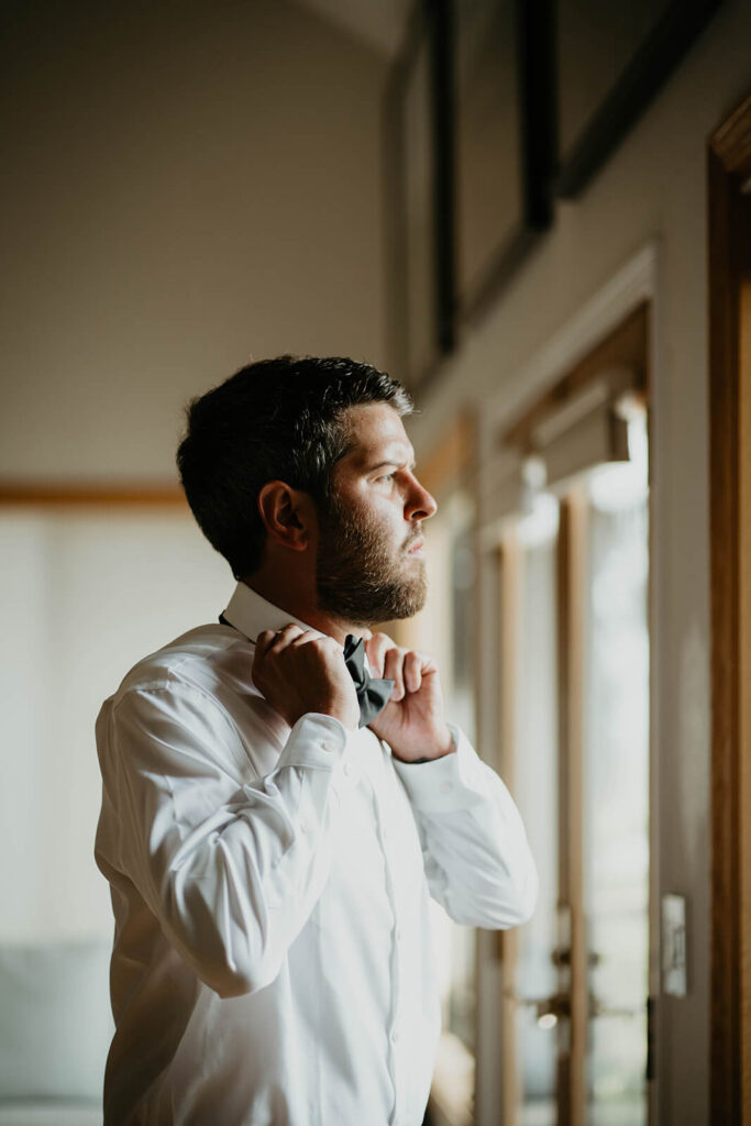 Groom adjusting bow tie 