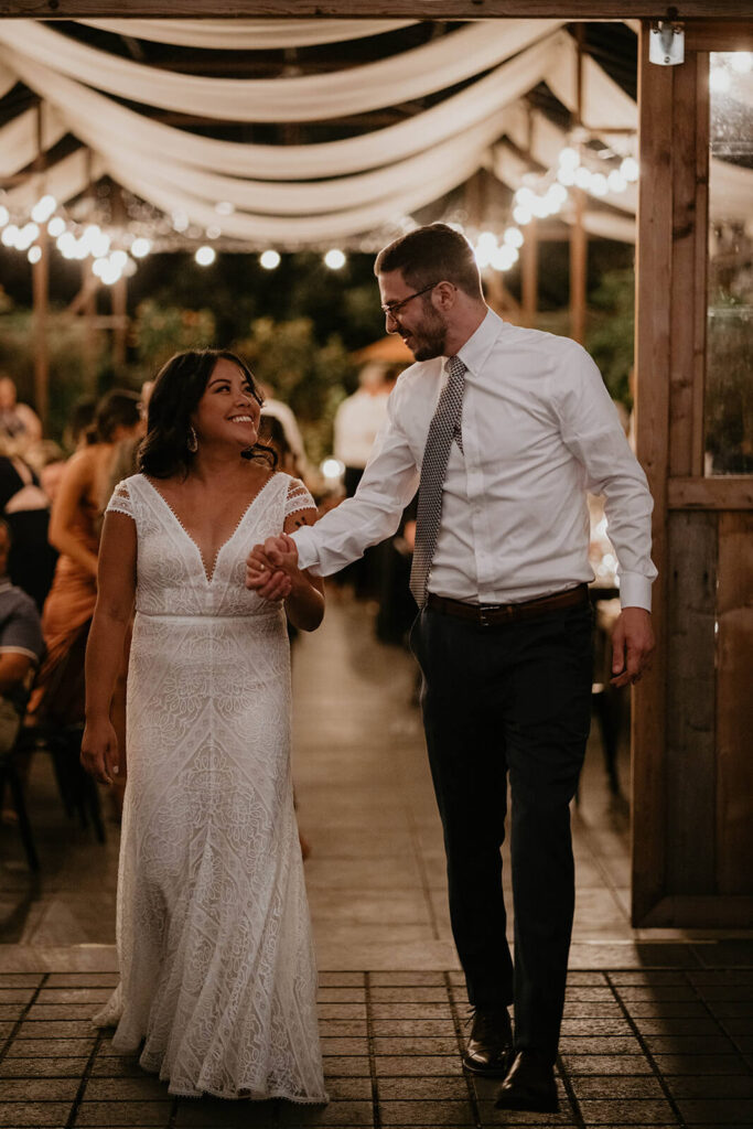 Bride and groom hold hands while entering the dance floor at botanical wedding reception