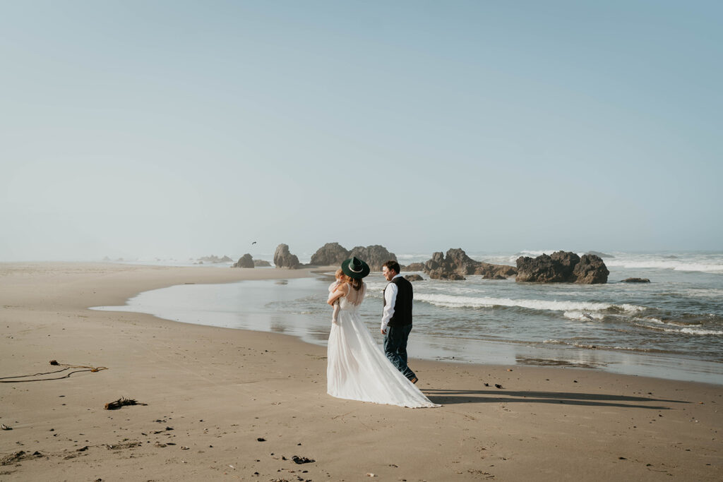 Couple walking across Oregon Coast beach with their baby 