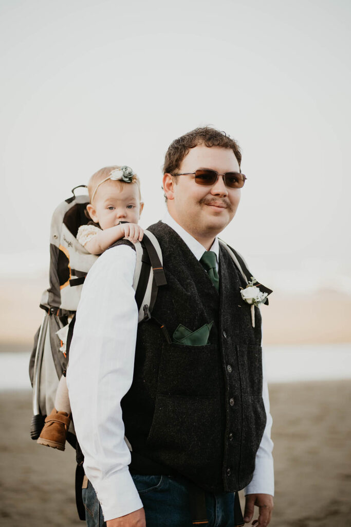 Groom carrying daughter in backpack