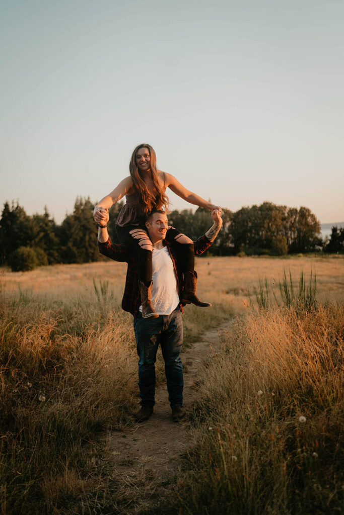 Woman riding on man's shoulders during Seattle engagement photos at Discovery Park