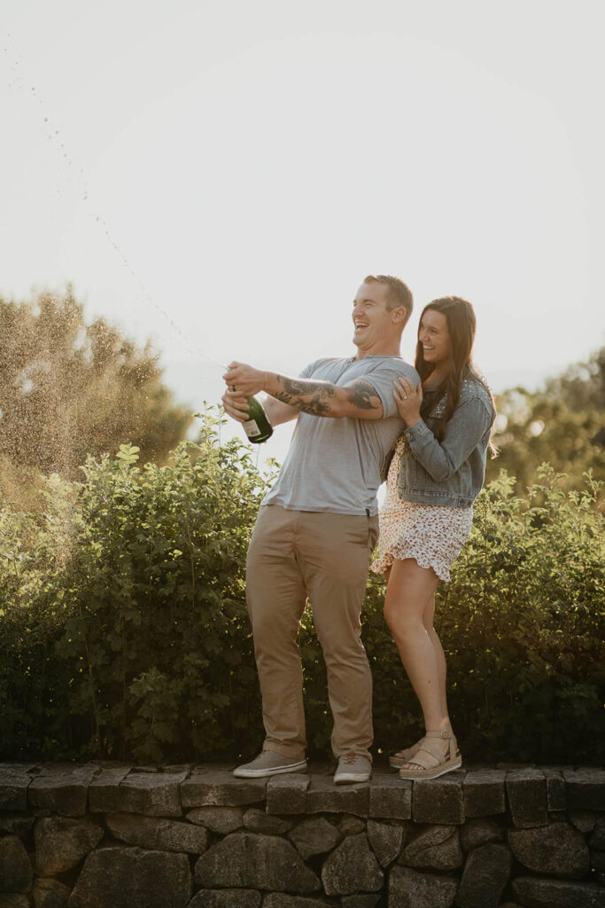 Couple popping champagne to celebrate at their Discovery Park engagement session in Seattle