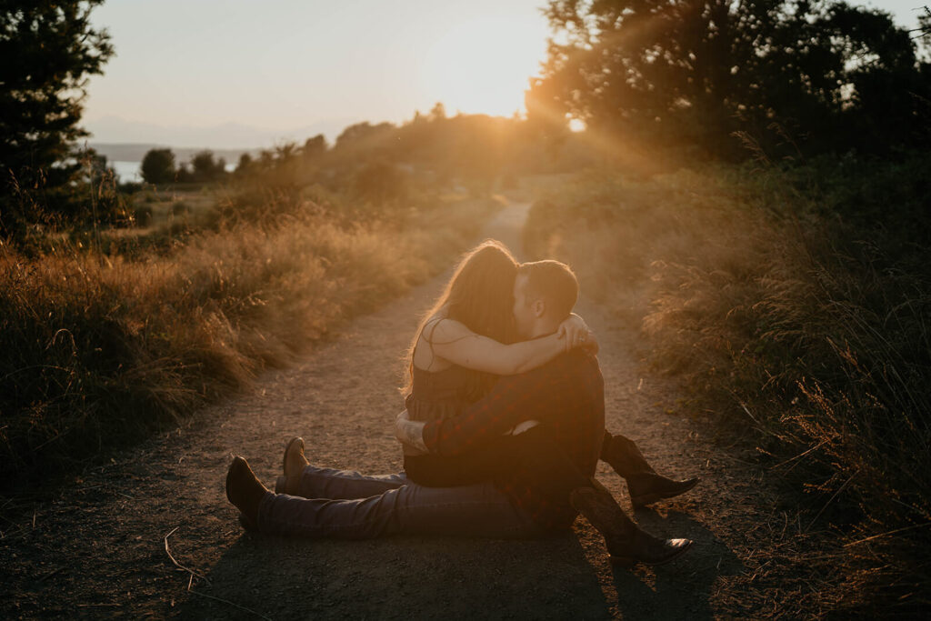 Couple sitting on the trail kissing during sunset engagement photos at Discovery Park