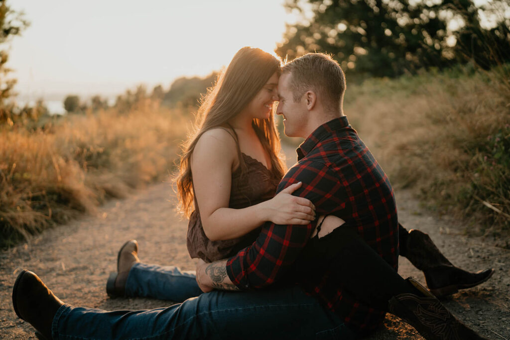 Couple sitting on the trail kissing during sunset engagement photos at Discovery Park