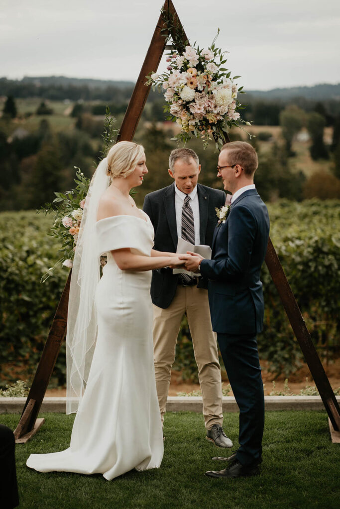 Bride and groom holding hands during outdoor wedding ceremony at Ponzi Vineyards