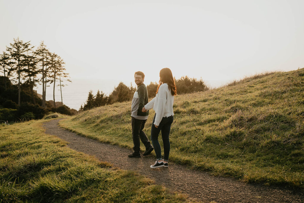 Couple holding hands walking along a trail during beach engagement photos