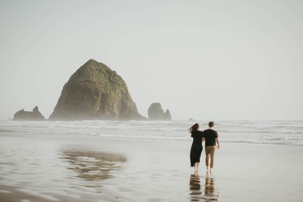 Couple holding hands, walking across Cannon Beach during their beach engagement photos