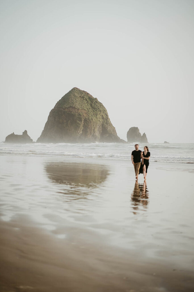 Couple holding hands, walking across Cannon Beach during their beach engagement photos