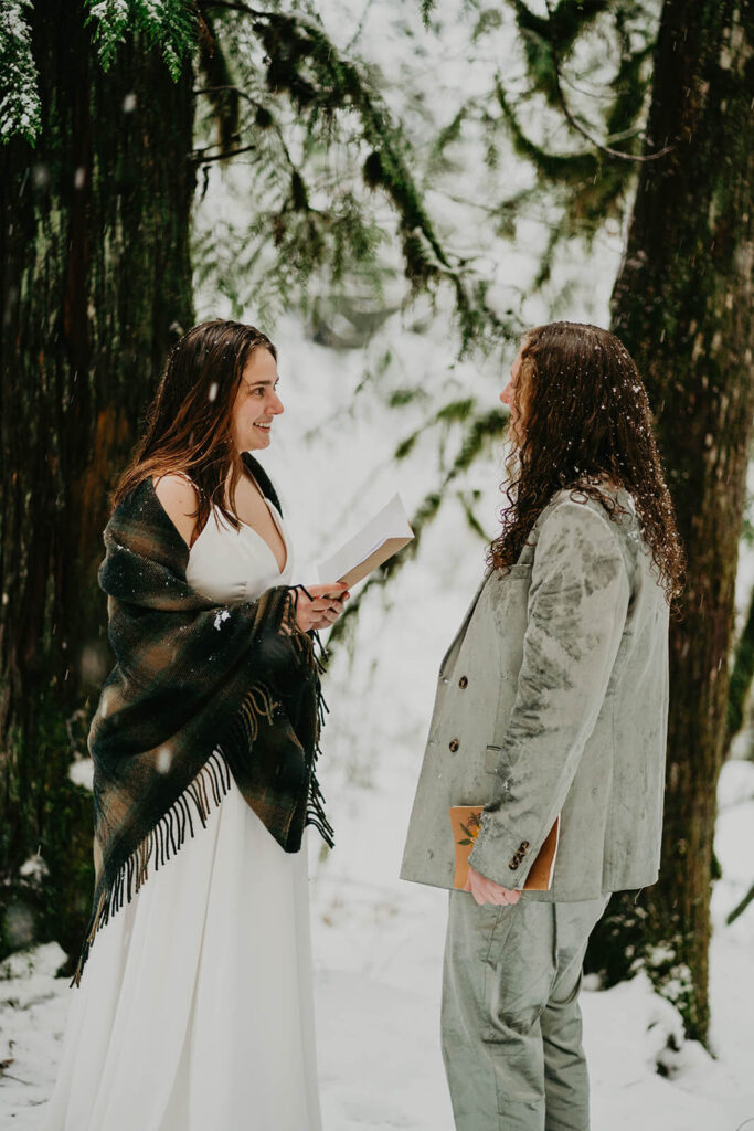 Two brides exchanging vows in the snow at winter wonderland cabin elopement in Oregon