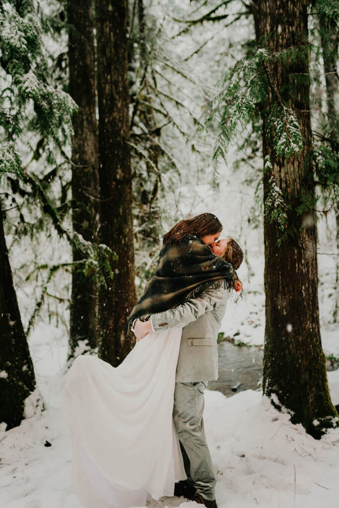 Two brides kissing in the snow at cozy Christmas cabin elopement in Oregon