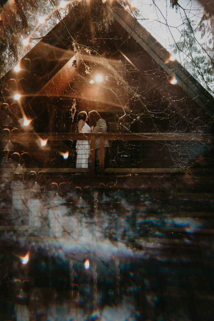 Two brides kissing at their dark moody wedding cabin in Oregon