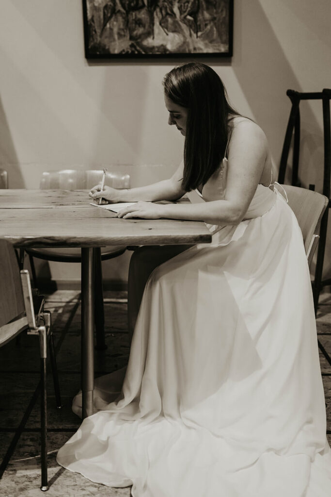 Bride wearing white wedding dress writing elopement vows in a cozy Christmas cabin