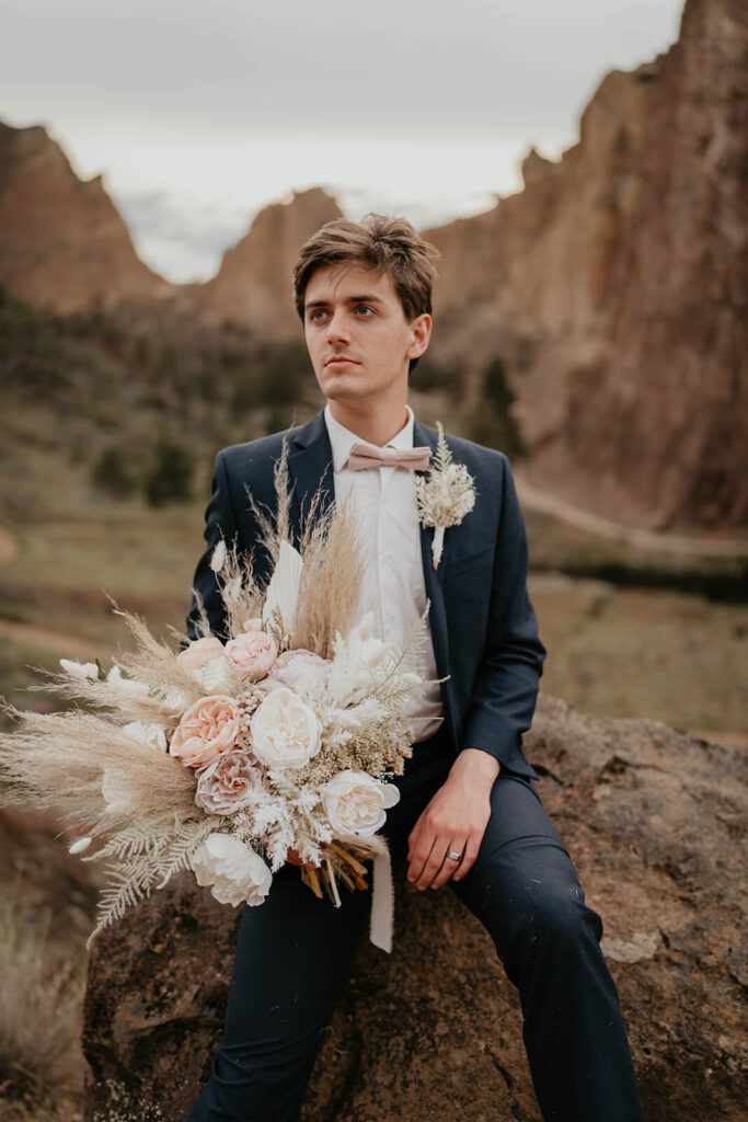 Groom in navy blue suit holding neutral wedding flower bouquet