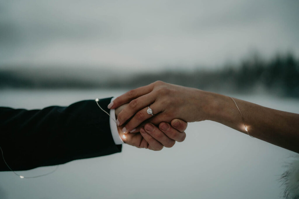 Couple holding hands with string lights wrapped around them in the snow