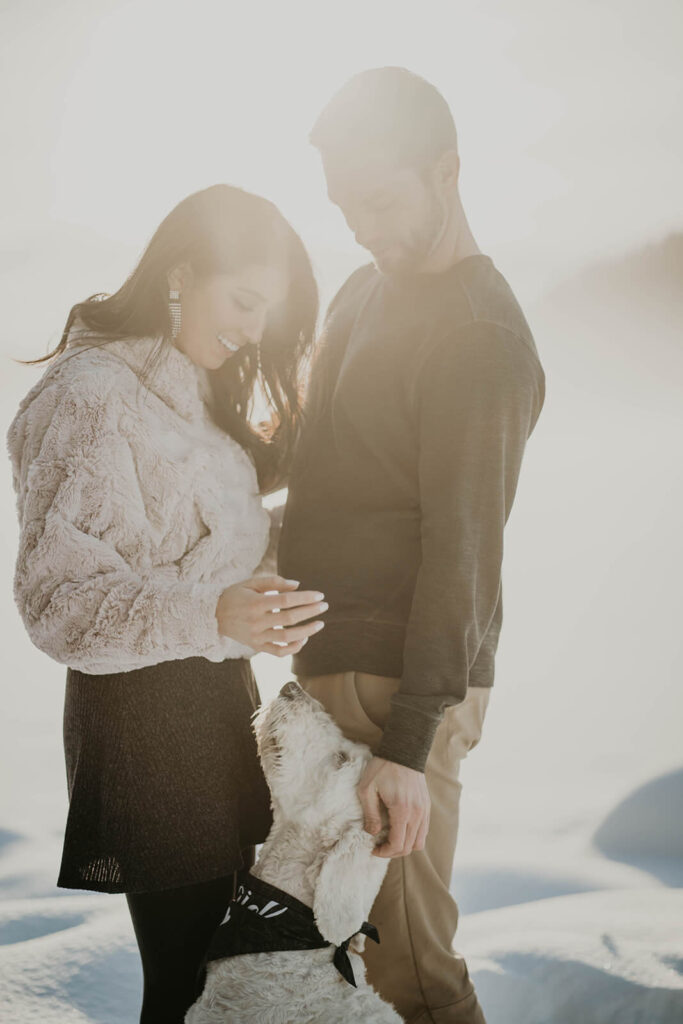 Couple petting white labradoodle during snow engagement photos at Trillium Lake