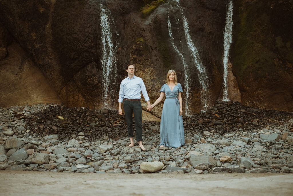 Couple holding hands in front of waterfall at Hug Point State Park