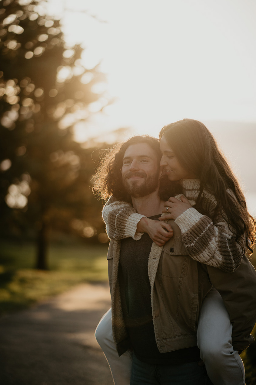 a boyfriend carrying his girlfriend while walking along a paved path during their engagement photo session.