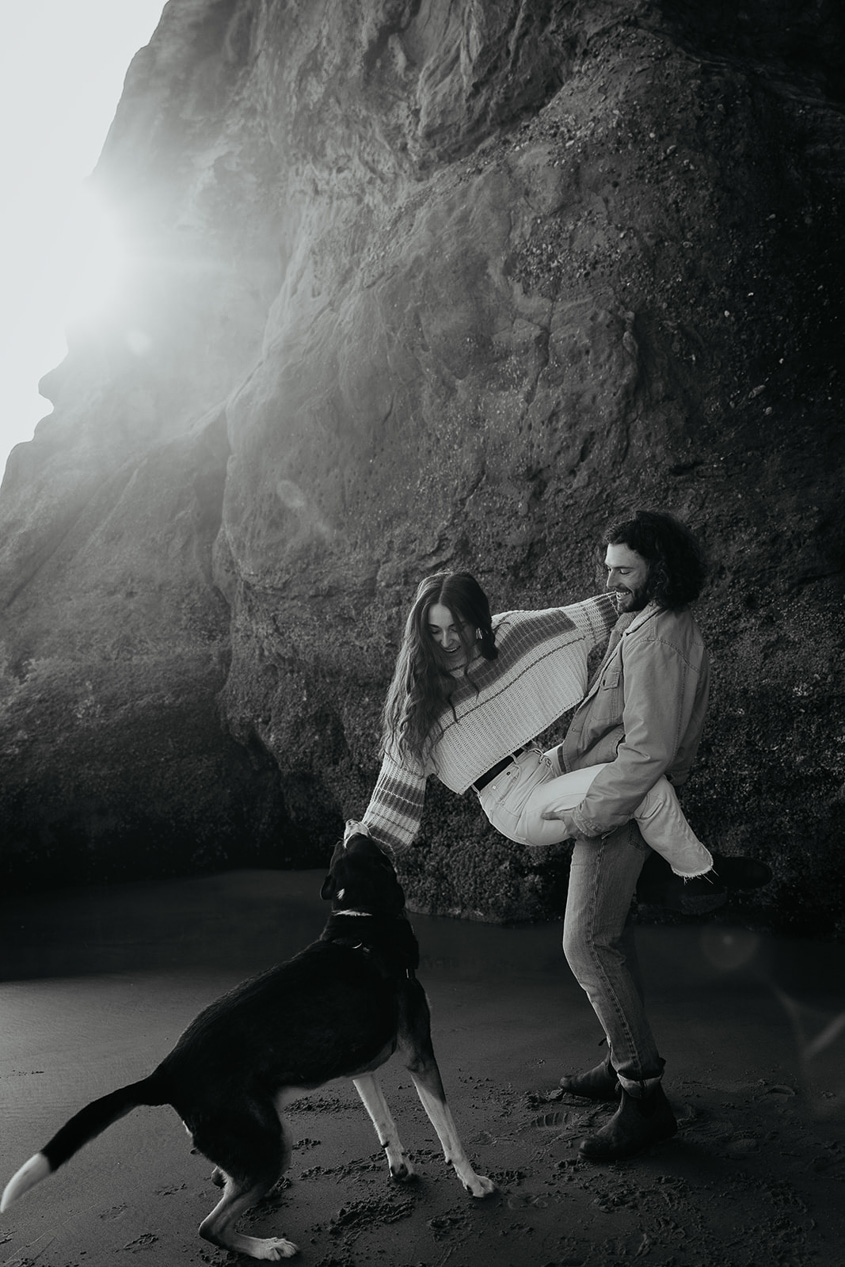a couple playing with their dog on the beach during their engagement photo session.