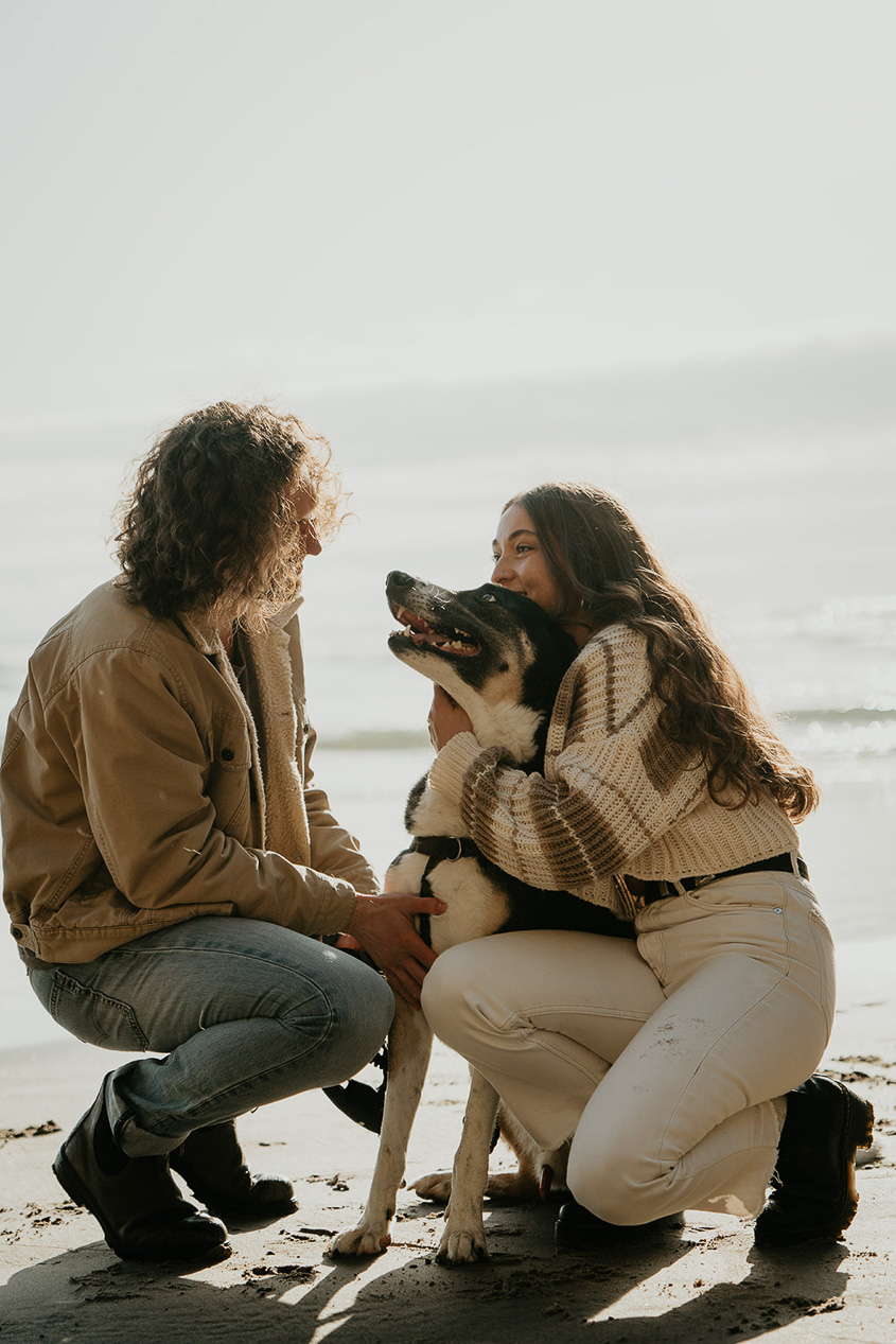 a couple cuddling with their dog on the Oregon coast.