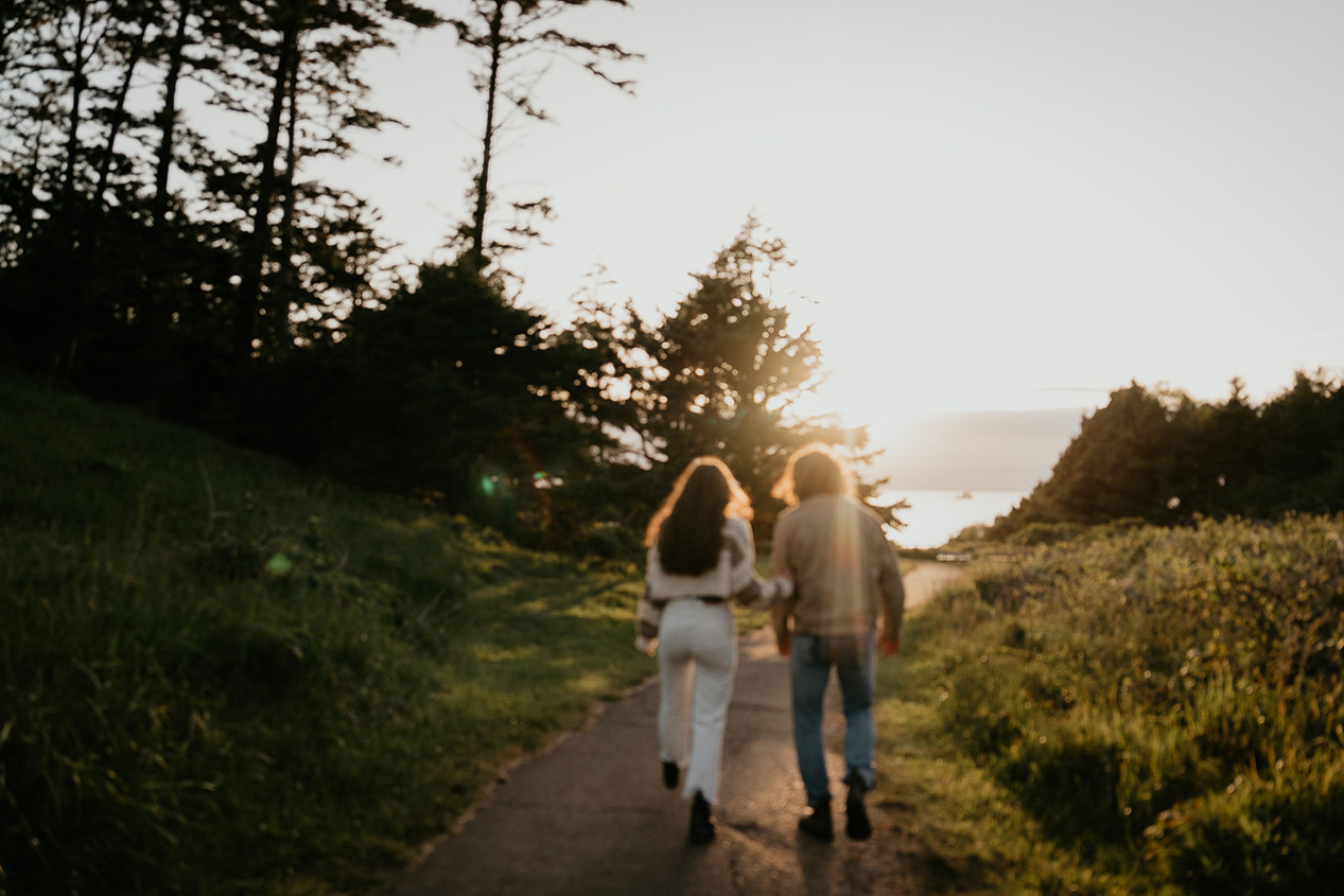 a couple holding hands running toward the beach at sunset during their engagement photo session.