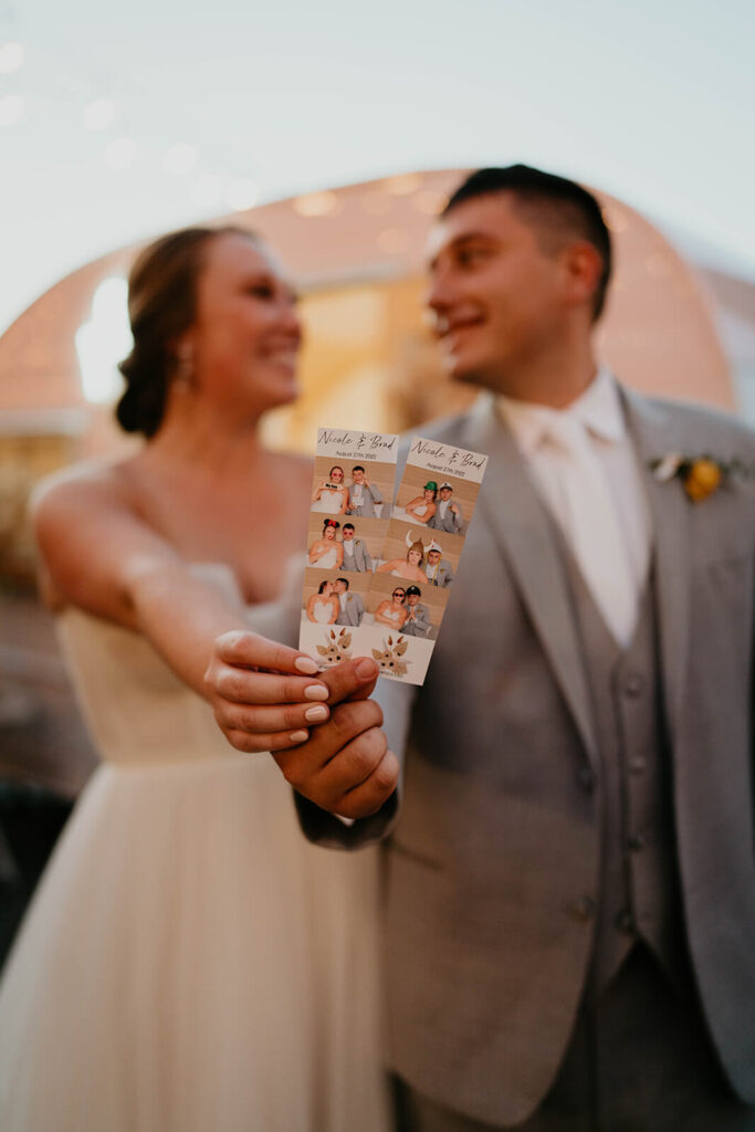 Bride and groom holding up photobooth photos 