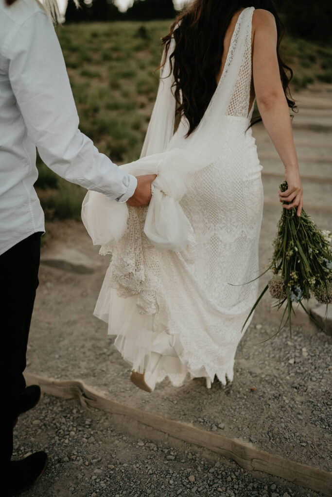 Bride helping other bride hold her dress as they walk through a trail at Sunrise, Mt Rainier