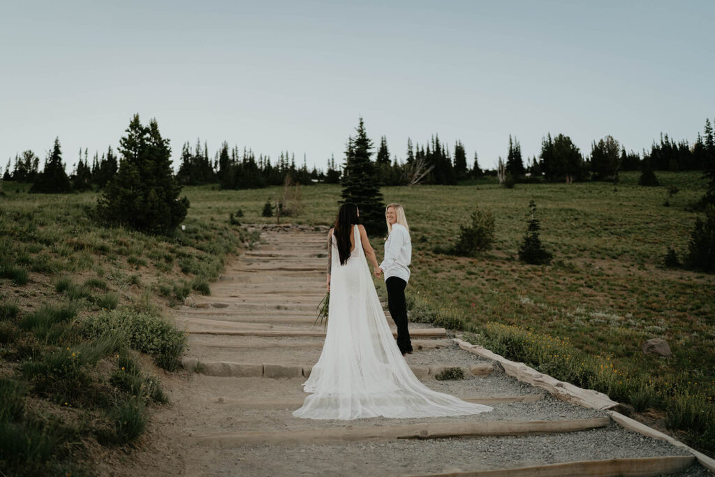 Two brides walk down a trail at Sunrise, Mt Rainier after their elopement ceremony