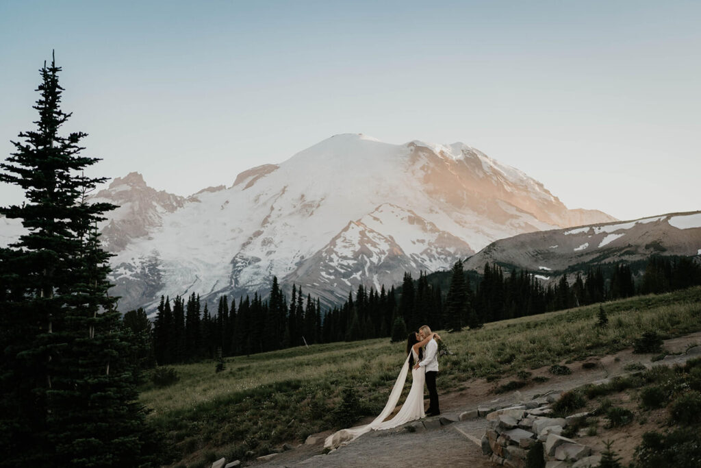 Two brides kissing on a trail in front of Mt Rainier