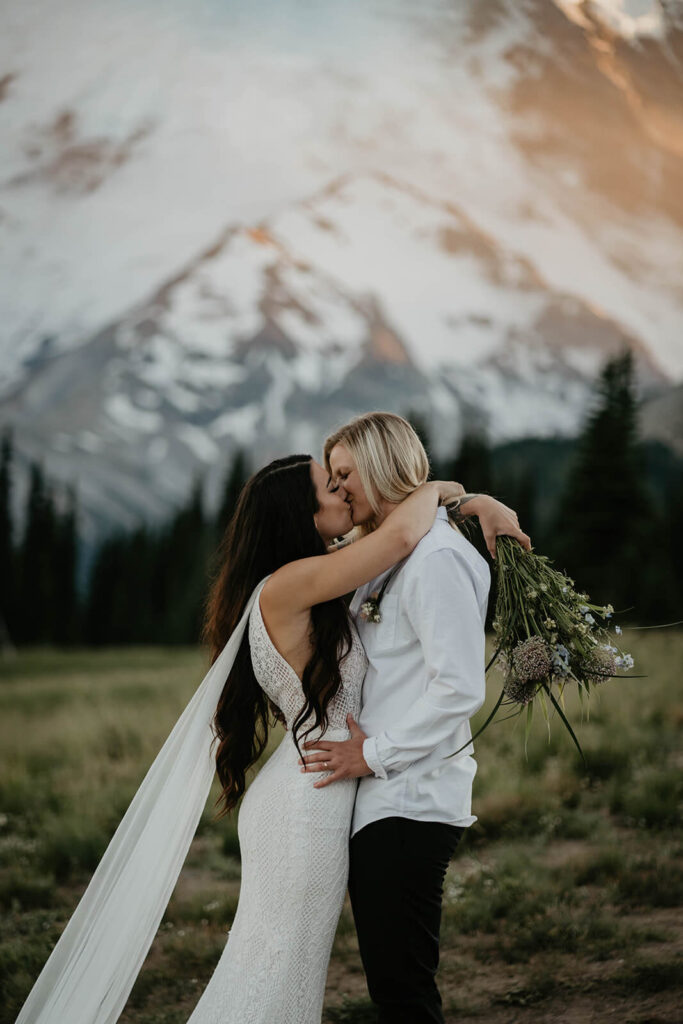 Two brides kissing on a trail in front of Mt Rainier