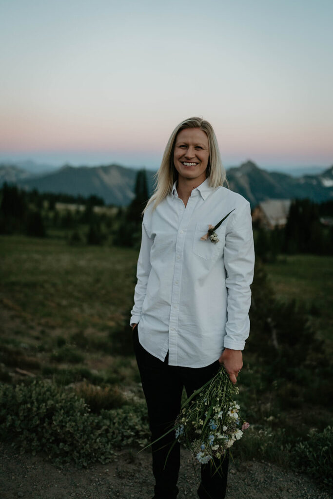 Bride wearing white button down and black pants, holding a bouquet of wildflowers