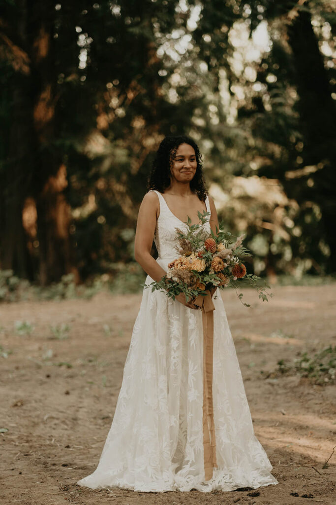 Bride holding bouquet of orange and green wedding flowers getting ready for first look at woodland themed wedding