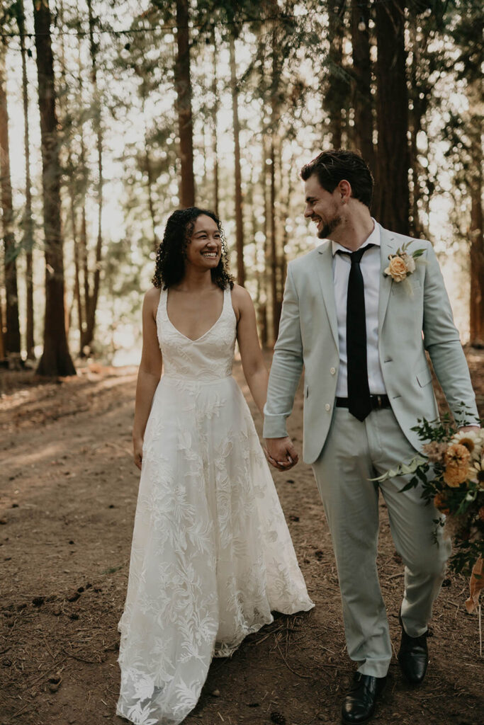 Bride and groom walking hand in hand through the forest at CedarVale Events wedding in Oregon