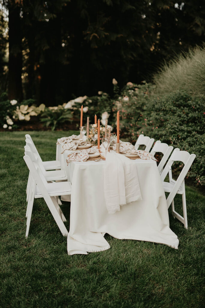 White reception table and chairs with orange and brown candlesticks and white place settings with patterned napkins