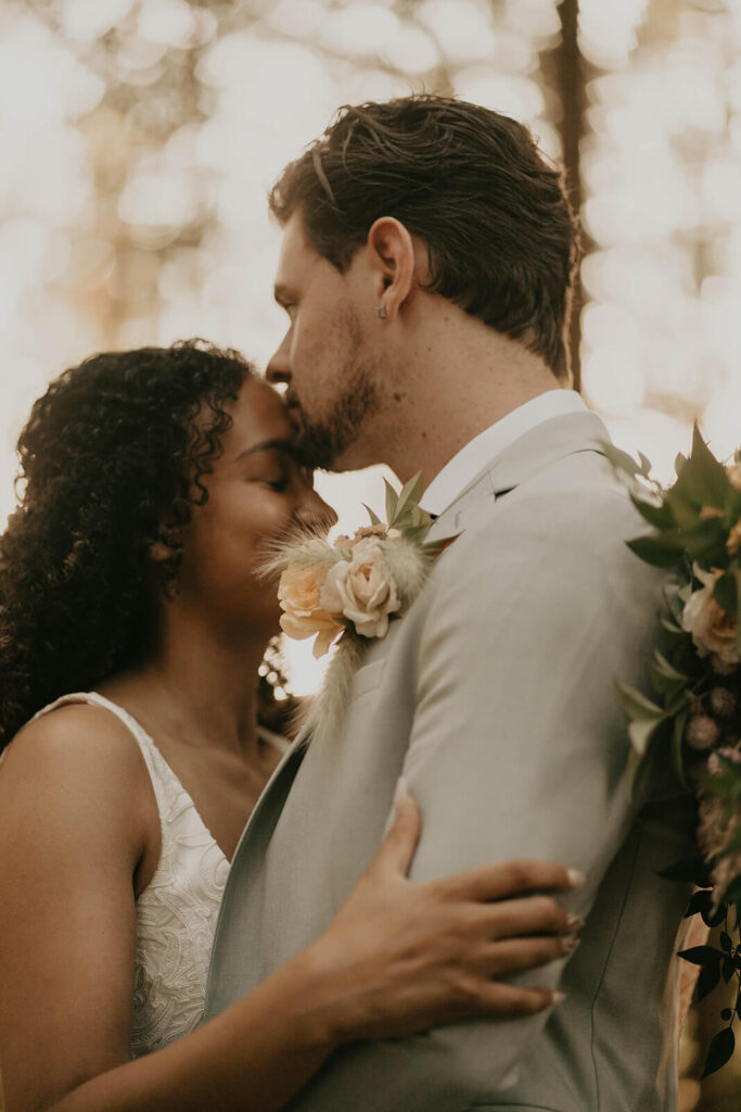 Groom kissing bride on the forehead at CedarVale Events woodland themed wedding 