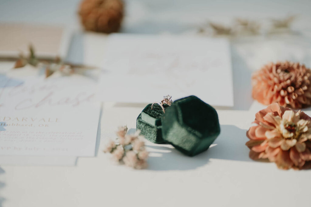 Diamond wedding bands in emerald green velvet ring box surrounded by orange flowers and white stationary