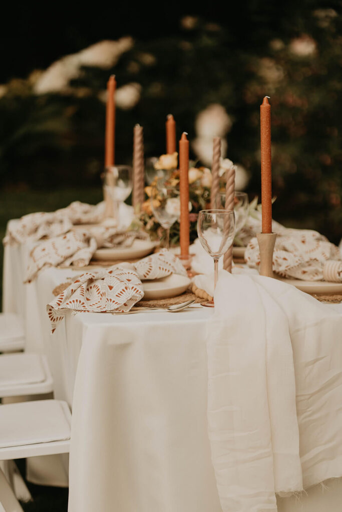 White reception table and chairs with orange and brown candlesticks and white place settings with patterned napkins