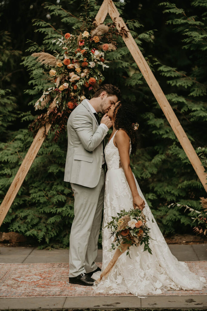 Bride and groom kiss during outdoor wedding ceremony at CedarVale Events woodland themed wedding