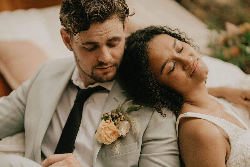 Bride rests her head on groom's shoulder while sitting in the woods for CedarVale Events wedding