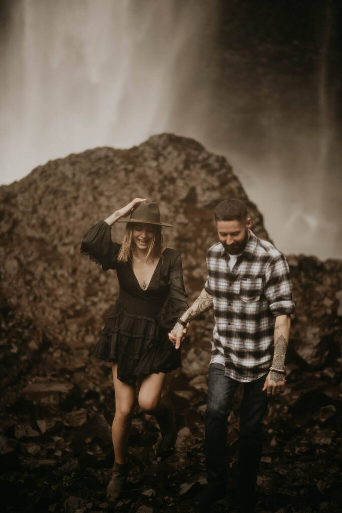 Couple holding hands and climbing down the rocks during their adventure engagement photos in Oregon