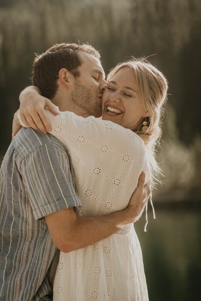 Woman hugging man while he kisses her during their adventure engagement photoshoot 