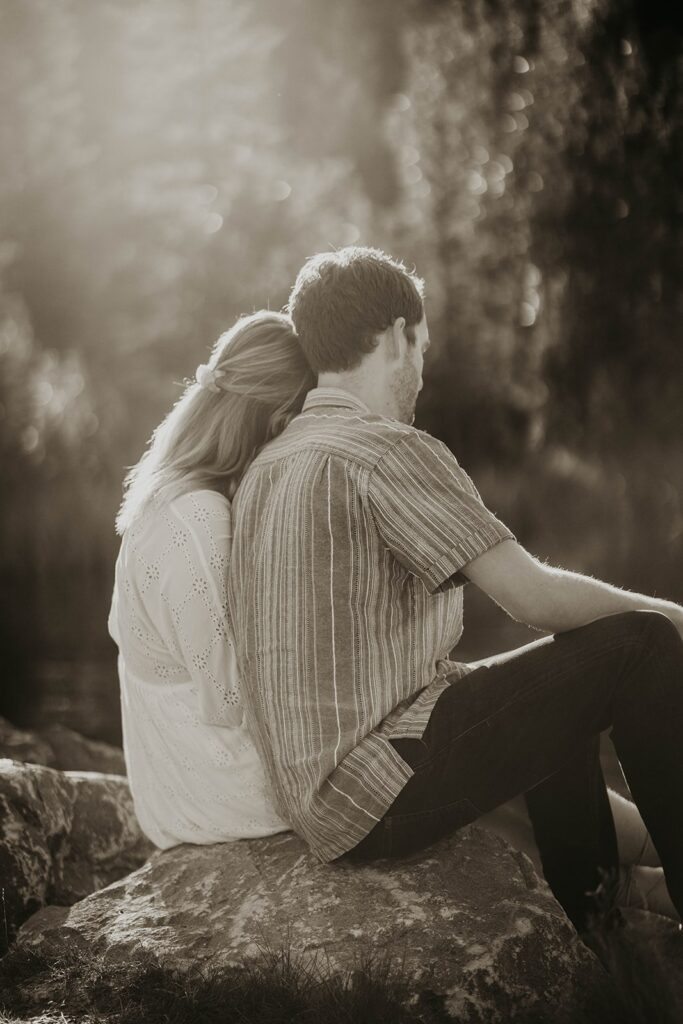 Woman resting her head on man's shoulder while sitting on a rock by the lake in Banff, Canada