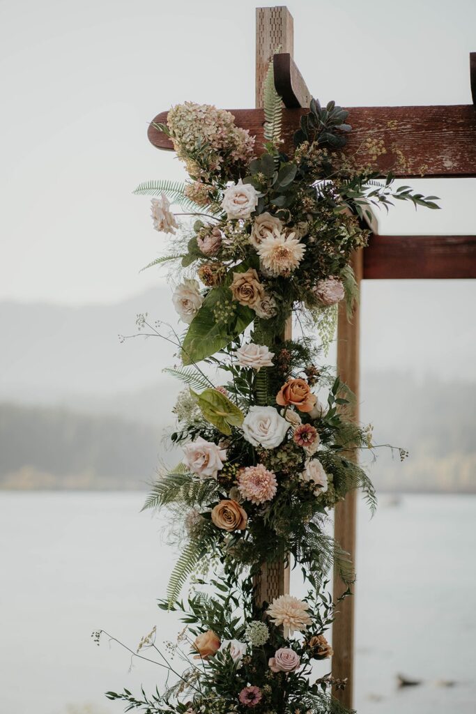 Pink, orange, and green floral arrangements hanging on a wood arch for Thunder Island wedding ceremony