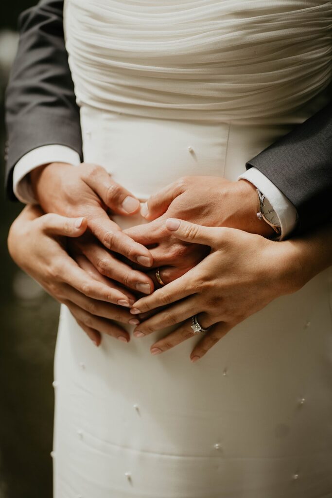 Bride and groom hold bride's pregnant belly at Asian wedding