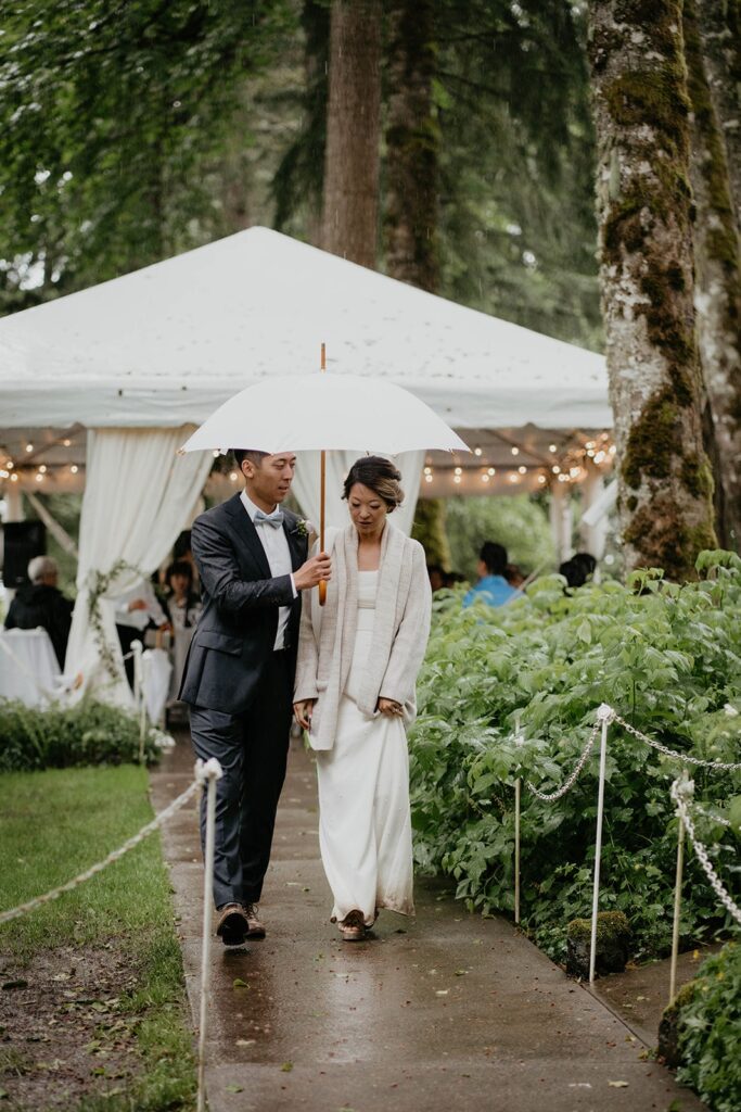 Bride and groom walk with an umbrella to their Bridal Veil Lakes wedding reception