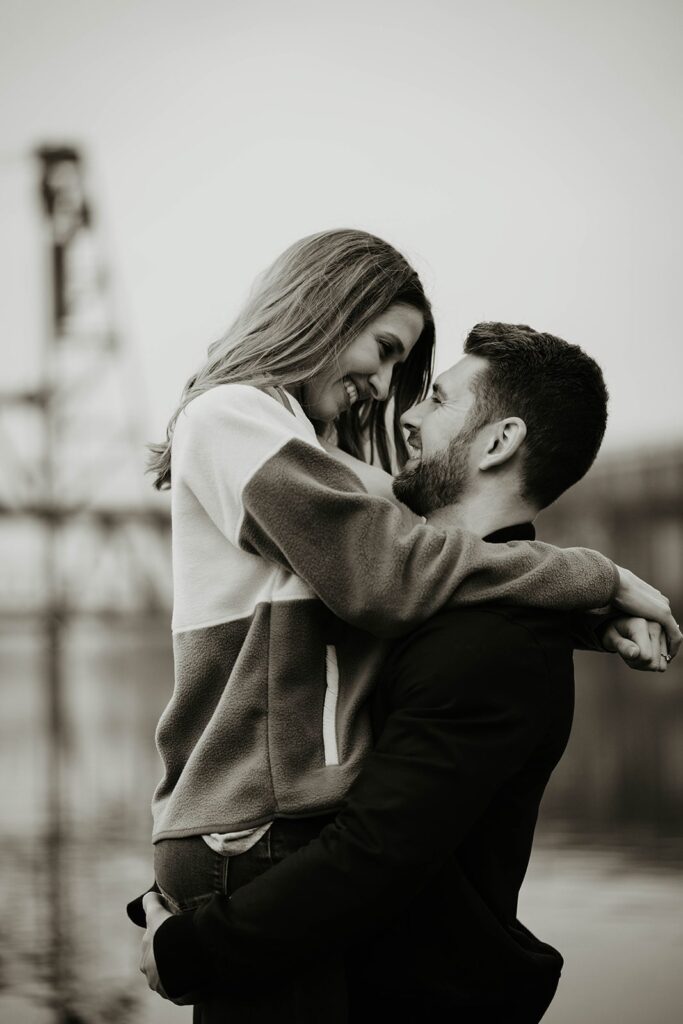 Couple hugging and smiling during Portland engagement photo session by the river