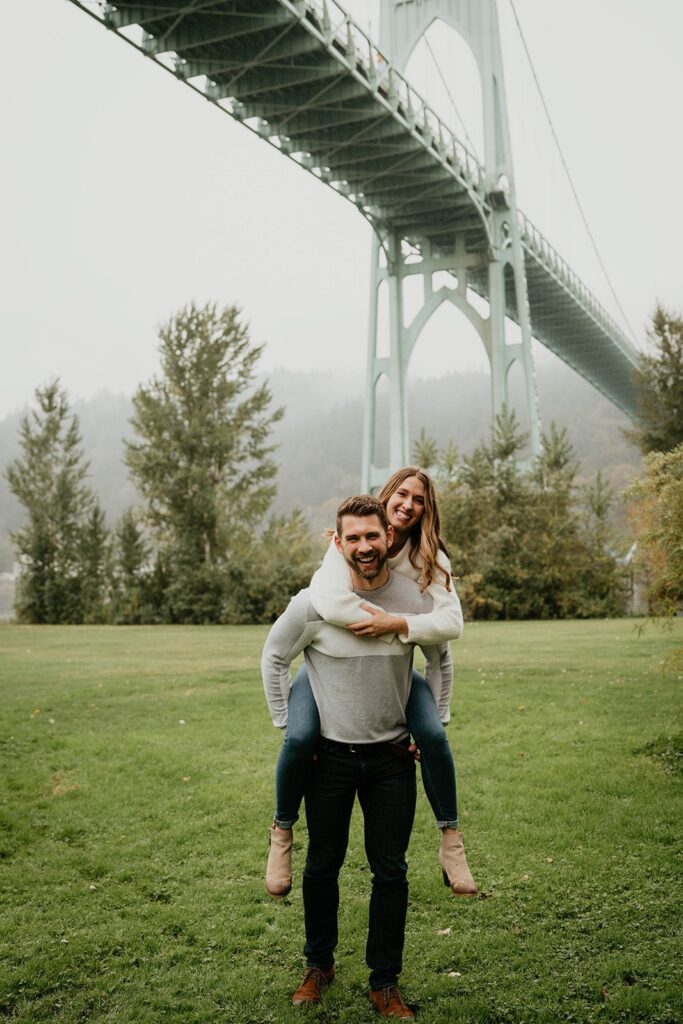 Woman riding on man's back during Cathedral Park, Oregon engagement photos