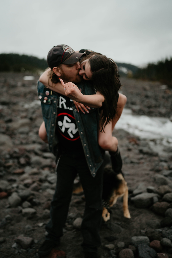 A couple kissing, with one being carried and showing off her engagement ring at White River West Sno-Park.